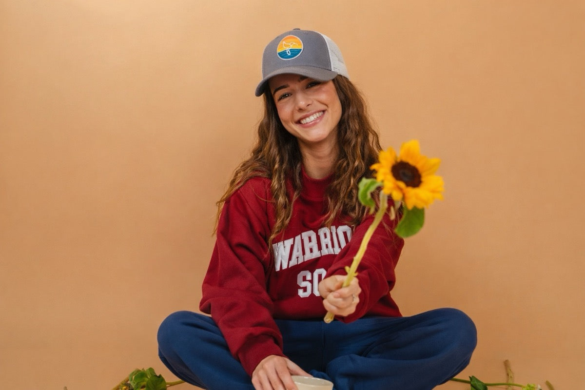 Hummingbird Sunrise Hat in Moon + Snow — model wearing gray and white hat with hummingbird sunrise logo, berry varsity, sunflower | Warrior Sol cancer support accessories