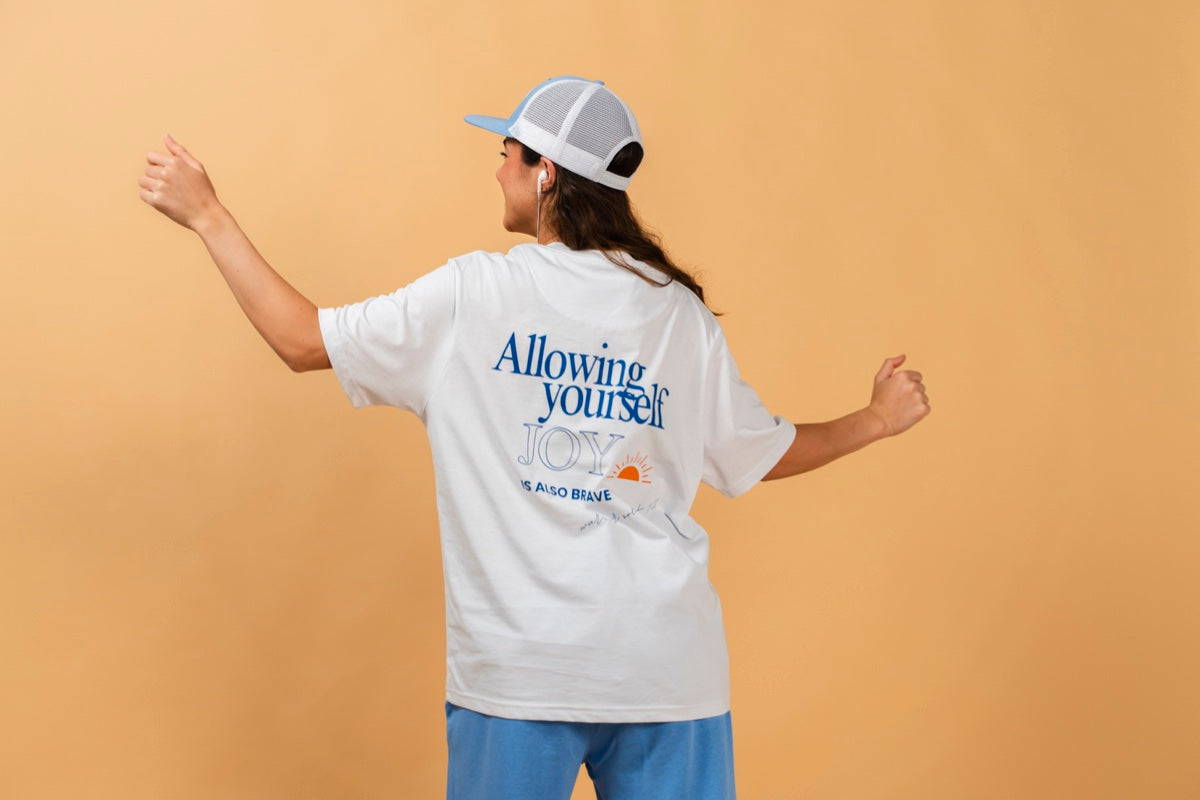 Warrior Sol Brave Series - Allowing yourself joy is also brave - female model back view wearing Snow White t-shirt with cap, warm gold campaign background