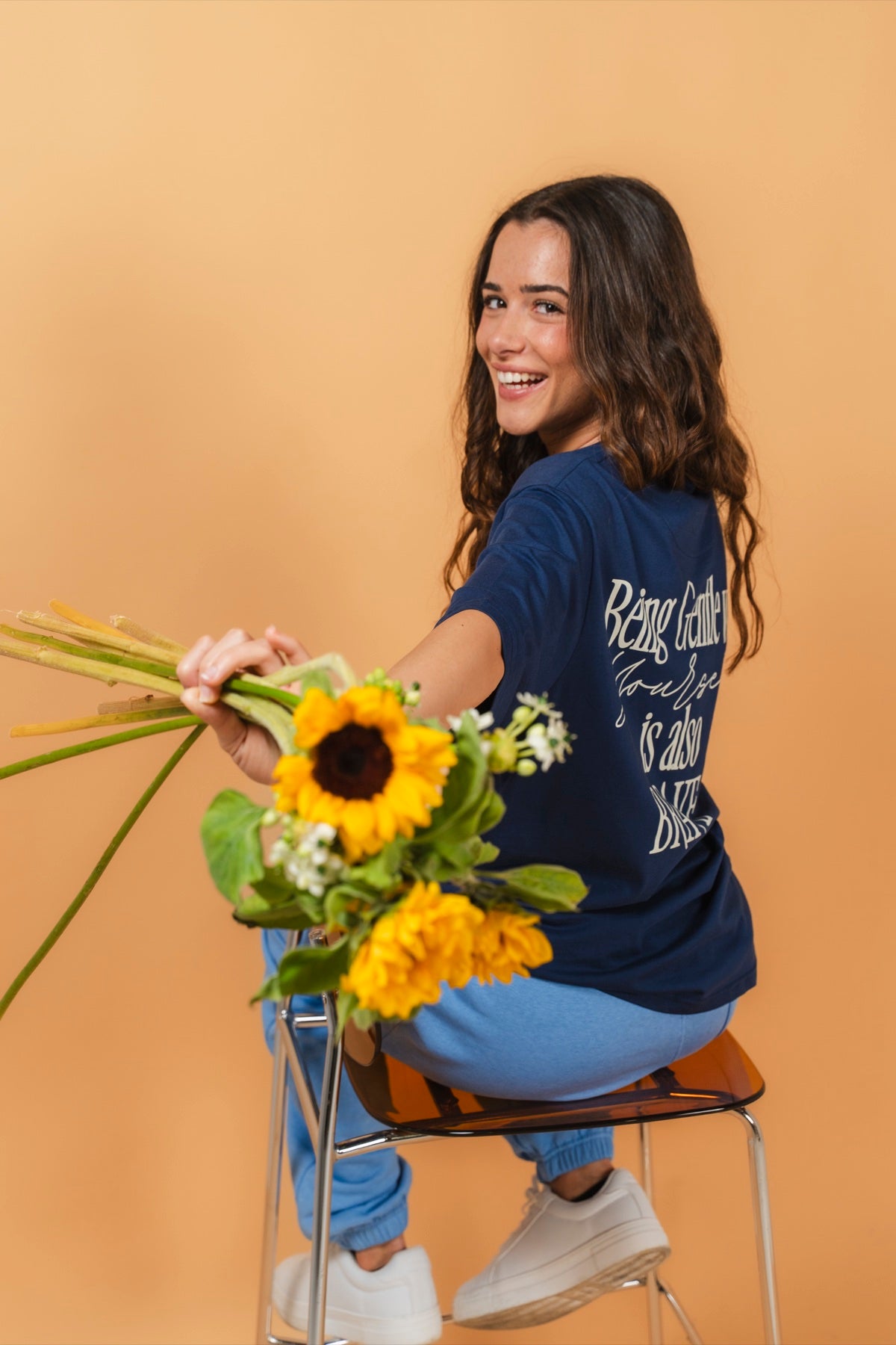 Warrior Sol Brave Series - Being gentle with yourself is also brave - female model smiling with sunflowers wearing Midnight Blue t-shirt, warm gold campaign background