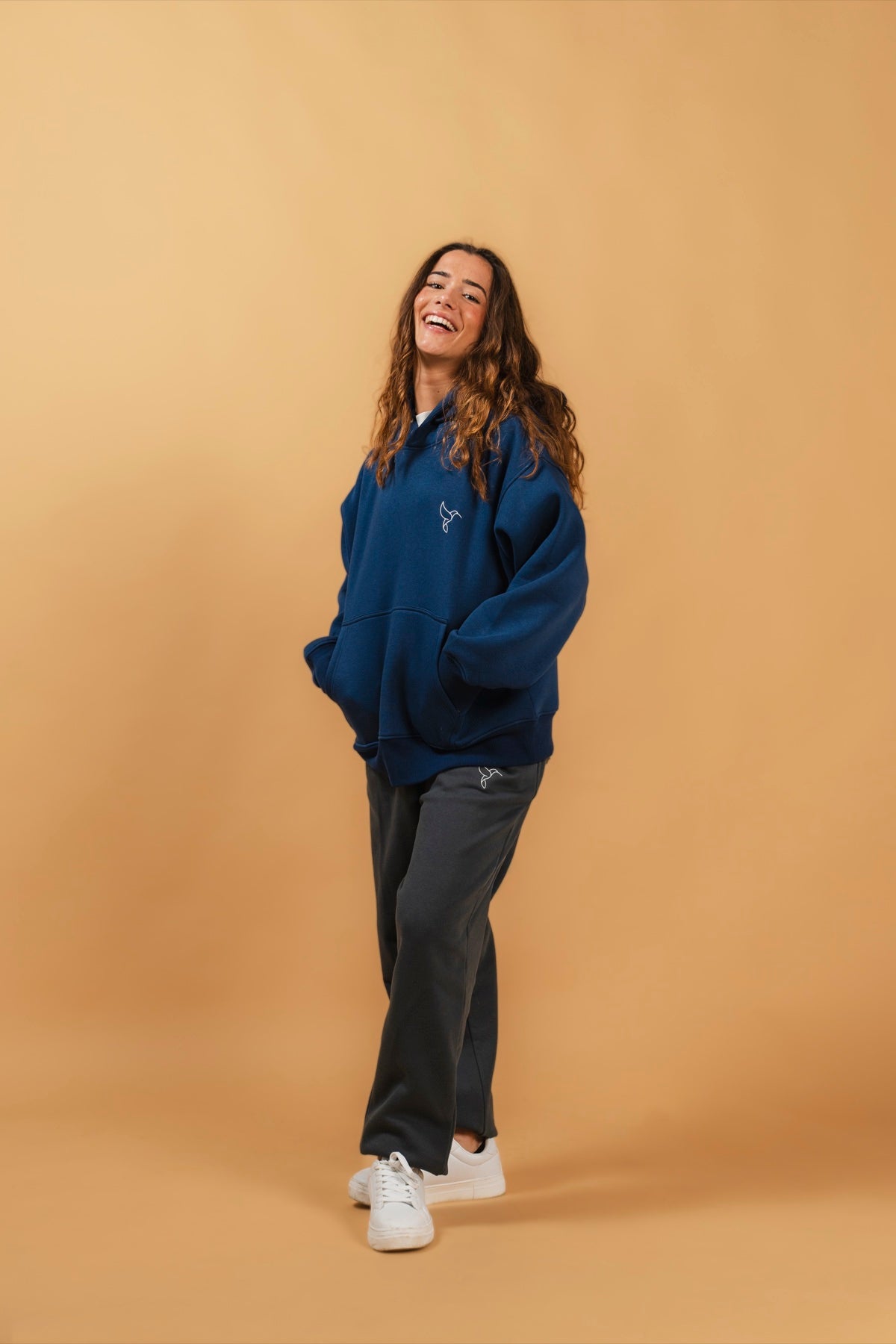 Warrior Sol Comfy Pullover Hoodie in Midnight Blue — campaign photo on gold background, model laughing in oversized midnight blue hoodie