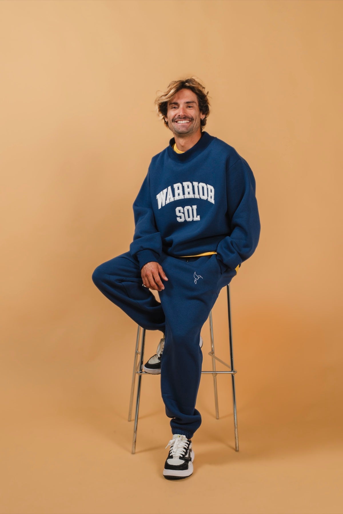 Warrior Sol All Day Sweatpants in Midnight Blue model on stool gold campaign background