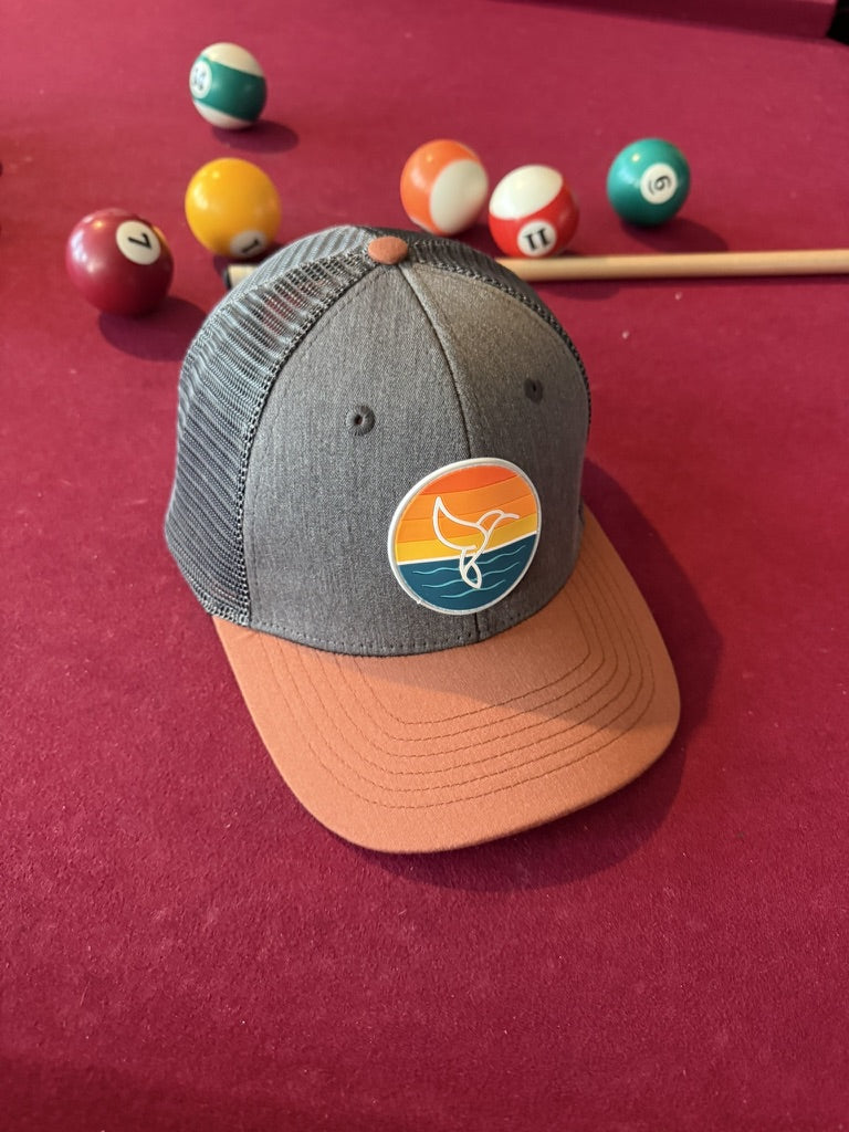 Warrior Sol Hummingbird Sunrise 6-panel trucker hat, Autumn + Charcoal colorway, front view with the sunset whale-tail patch