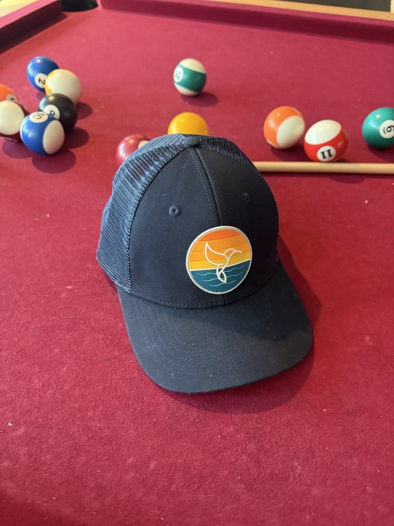 Warrior Sol Hummingbird Sunrise 6-panel trucker hat, Midnight colorway, front view with the sunset whale-tail patch