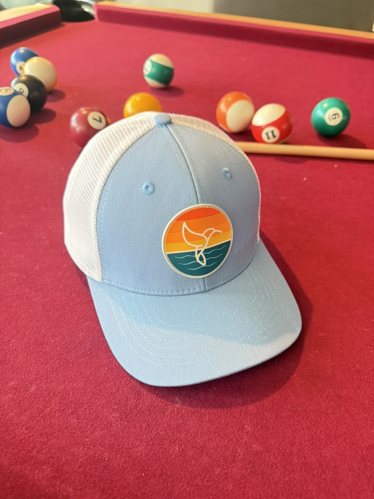 Warrior Sol Hummingbird Sunrise 6-panel trucker hat, Sky + Snow colorway, front view with the sunset whale-tail patch